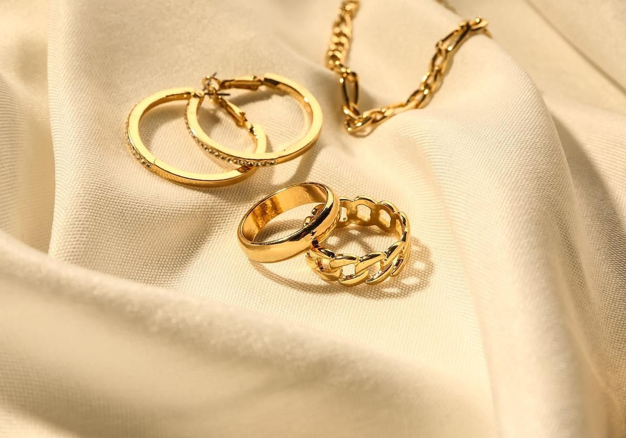 A collection of golden rings and a chain displayed on a white cloth, highlighting their shine and intricate designs.
